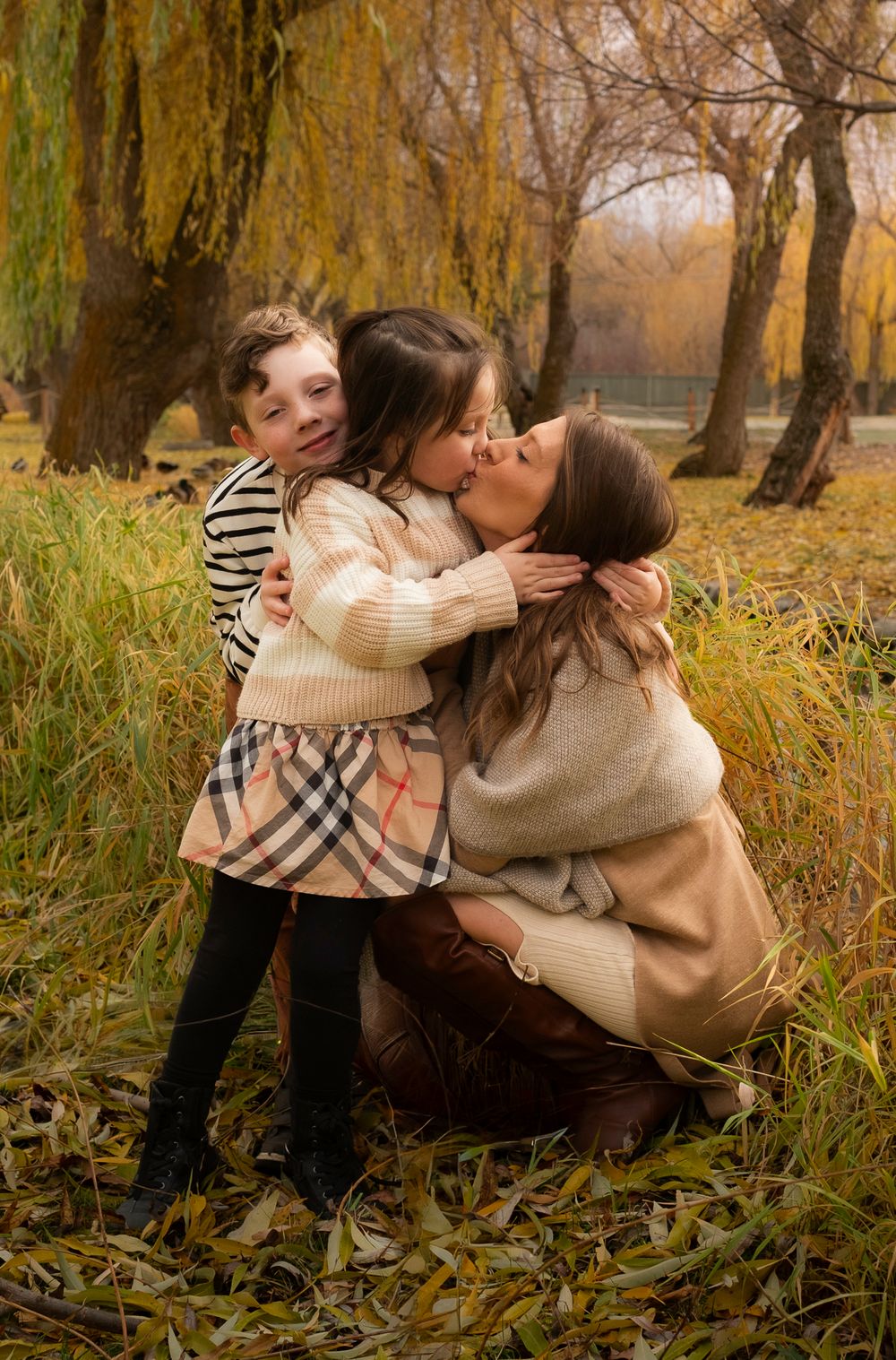 Couple embracing in autumn park with fallen leaves and willow trees in warm golden light.