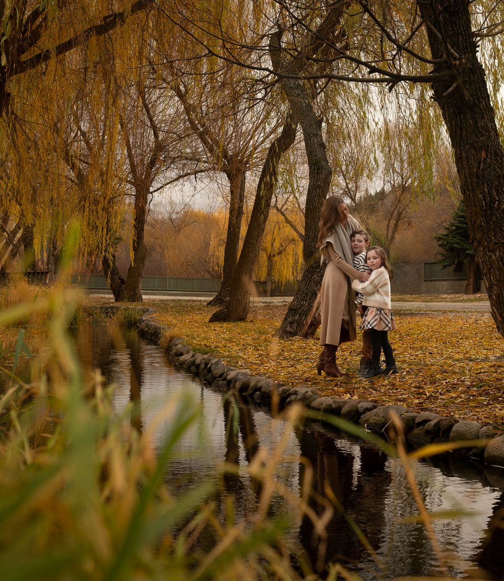 Romantic scene by stream in autumn park with willow trees and fallen leaves.