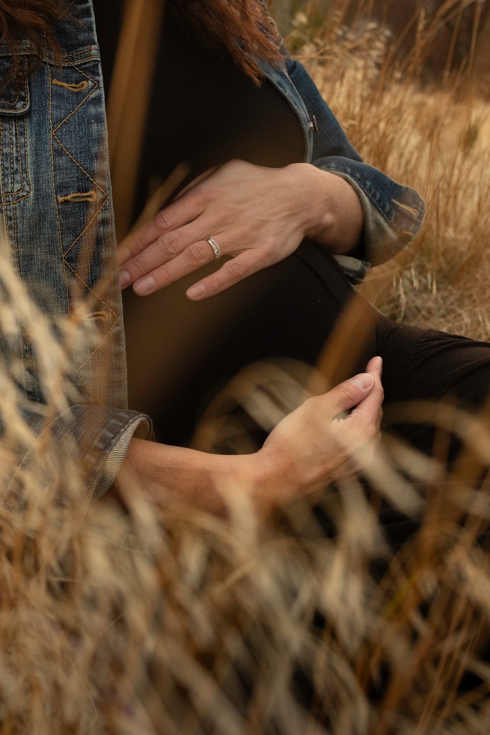 Artistic close-up of hands against dried grass background during outdoor photoshoot.