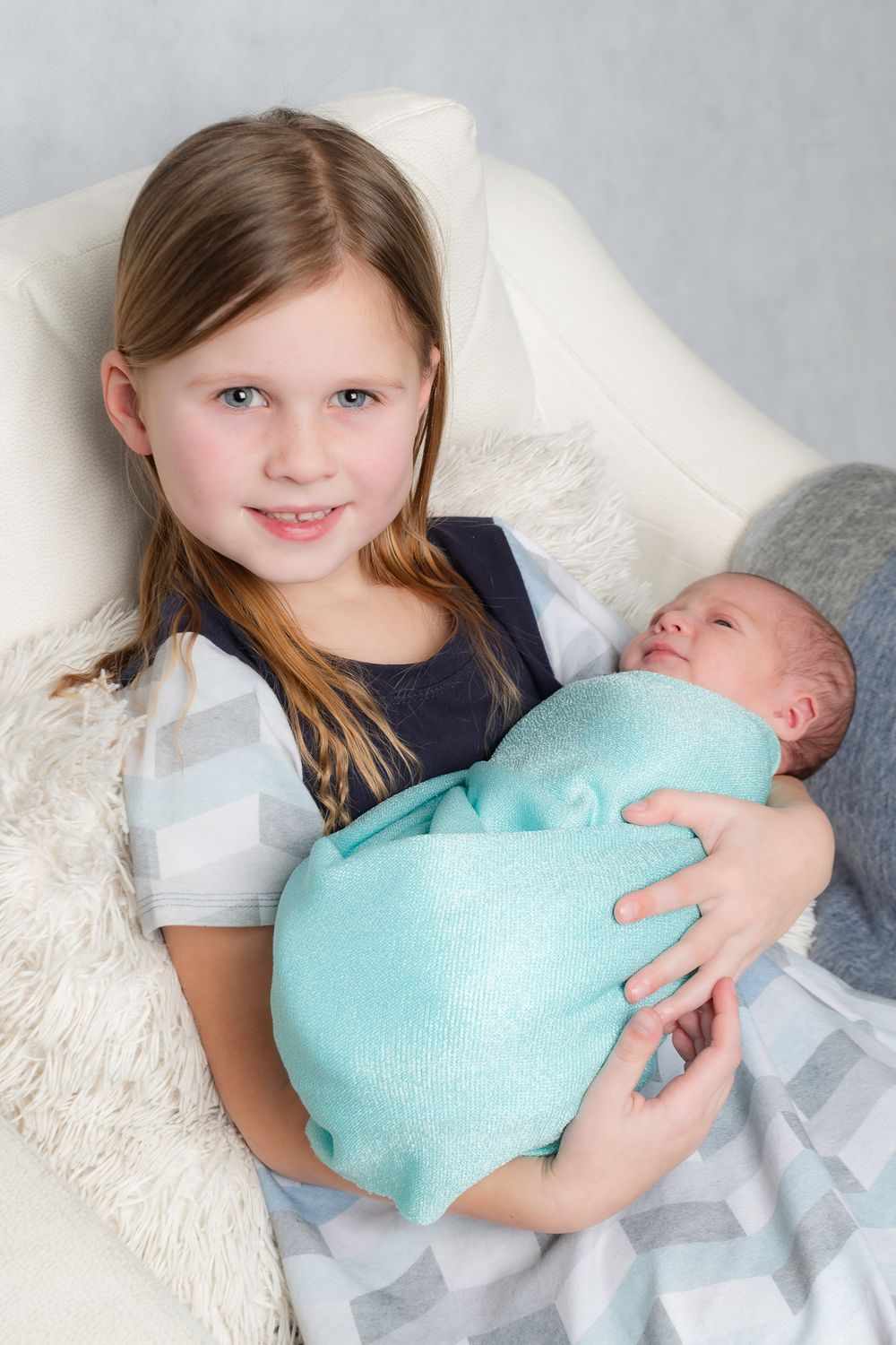 Sibling portrait series showing a young girl holding and bonding with a newborn baby in mint blanket.