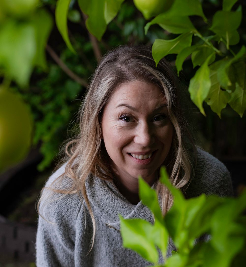A person peeks through citrus tree leaves with a cheerful expression.