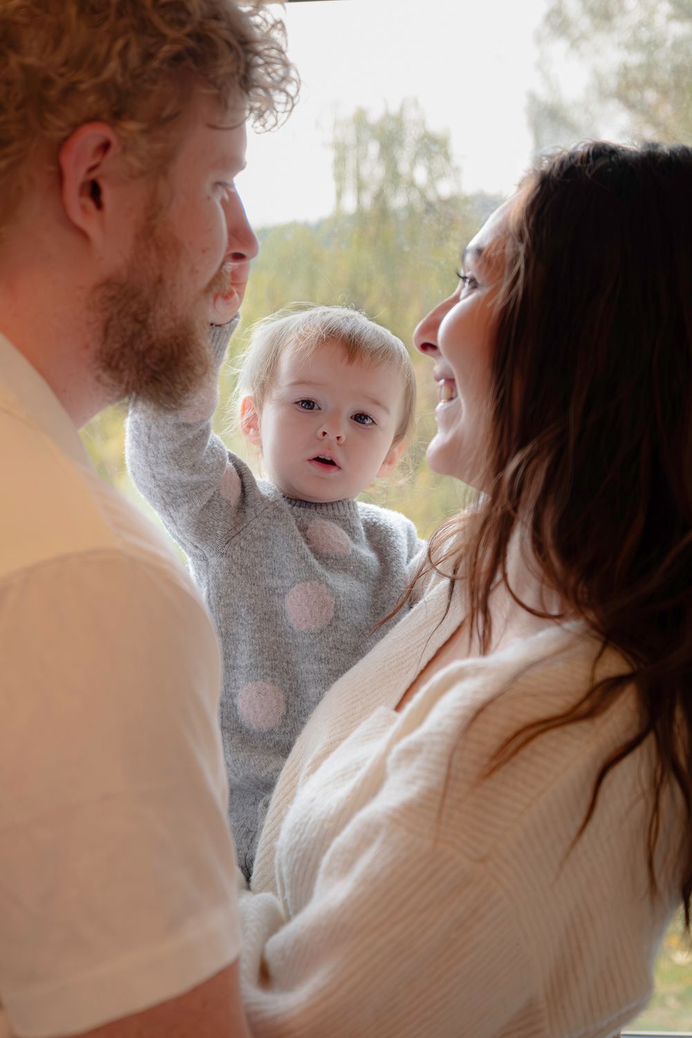 Family moment captured indoors with soft natural lighting and white sweaters.
