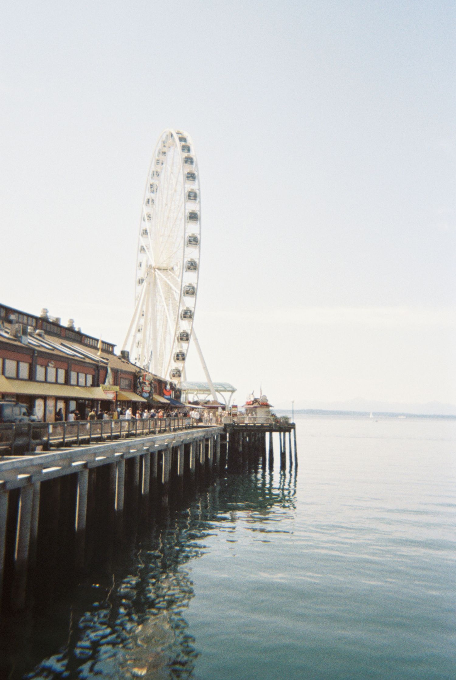 A panoramic view of Seattle's waterfront pier with the Great Wheel ferris wheel against a cloudy sky and calm waters.
