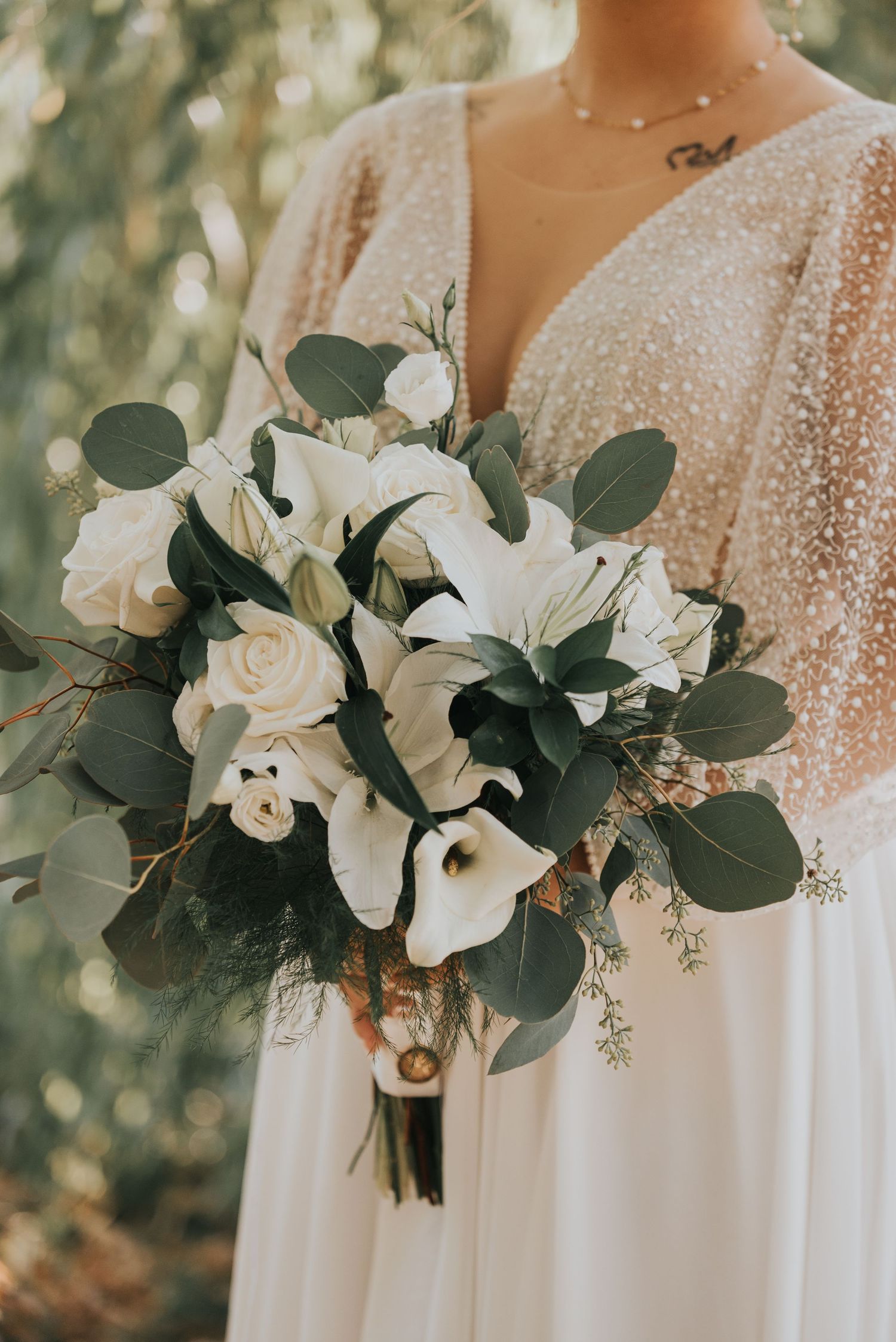 Close-up details of white wedding bouquets with lilies, eucalyptus leaves and sparkly bridal gown bodices in natural light.