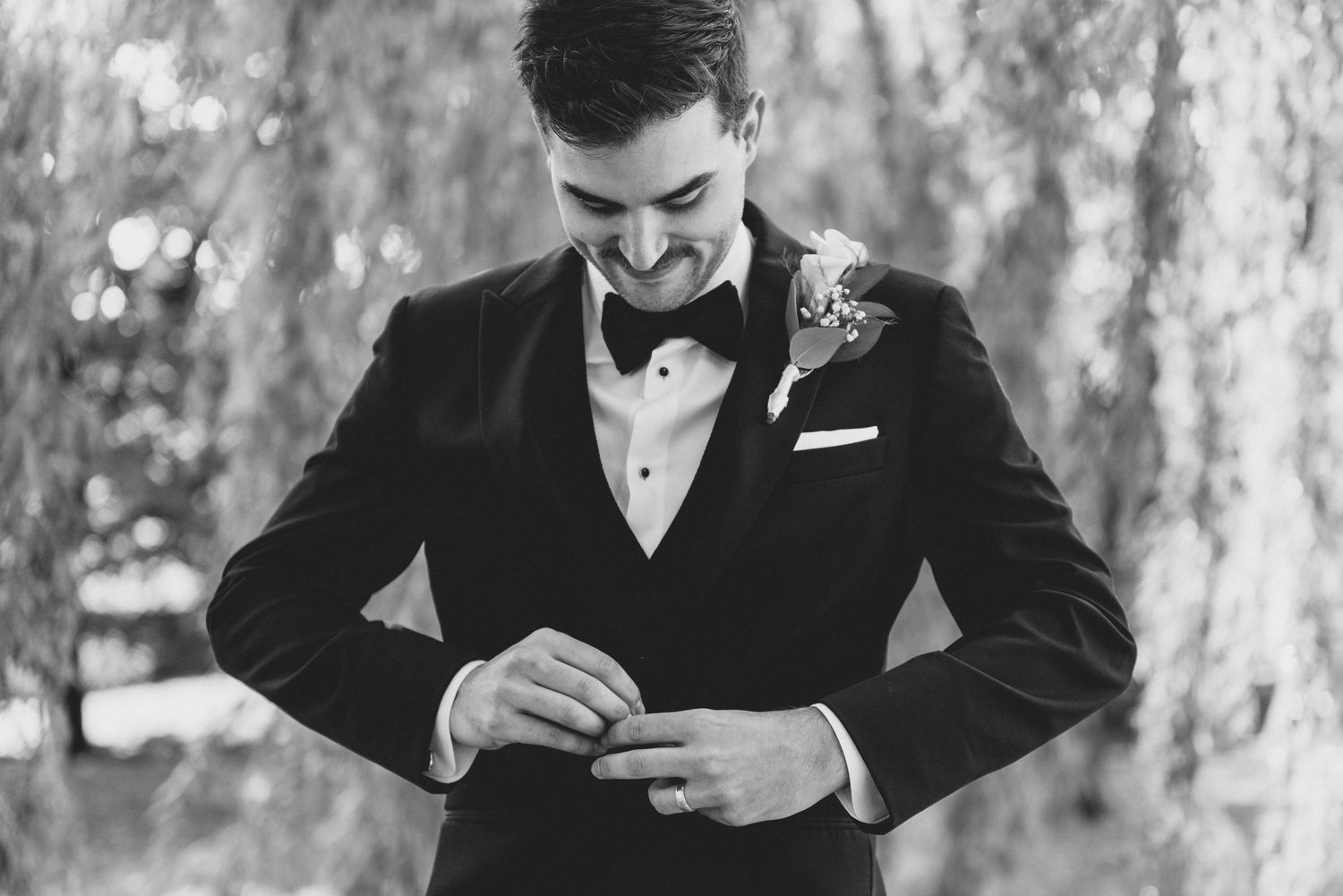 Black and white photo of groomsmen in formal attire preparing for wedding ceremony.