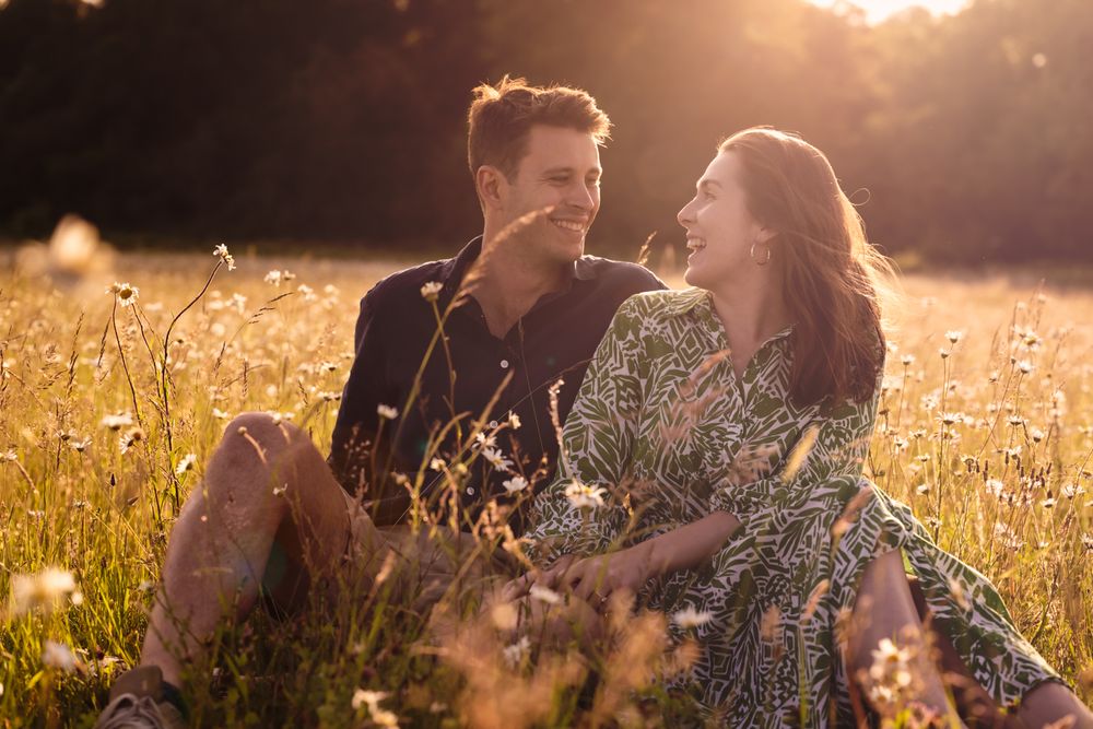 Couple sits together in a golden sunlit meadow with dandelions during sunset creating a dreamy romantic atmosphere.