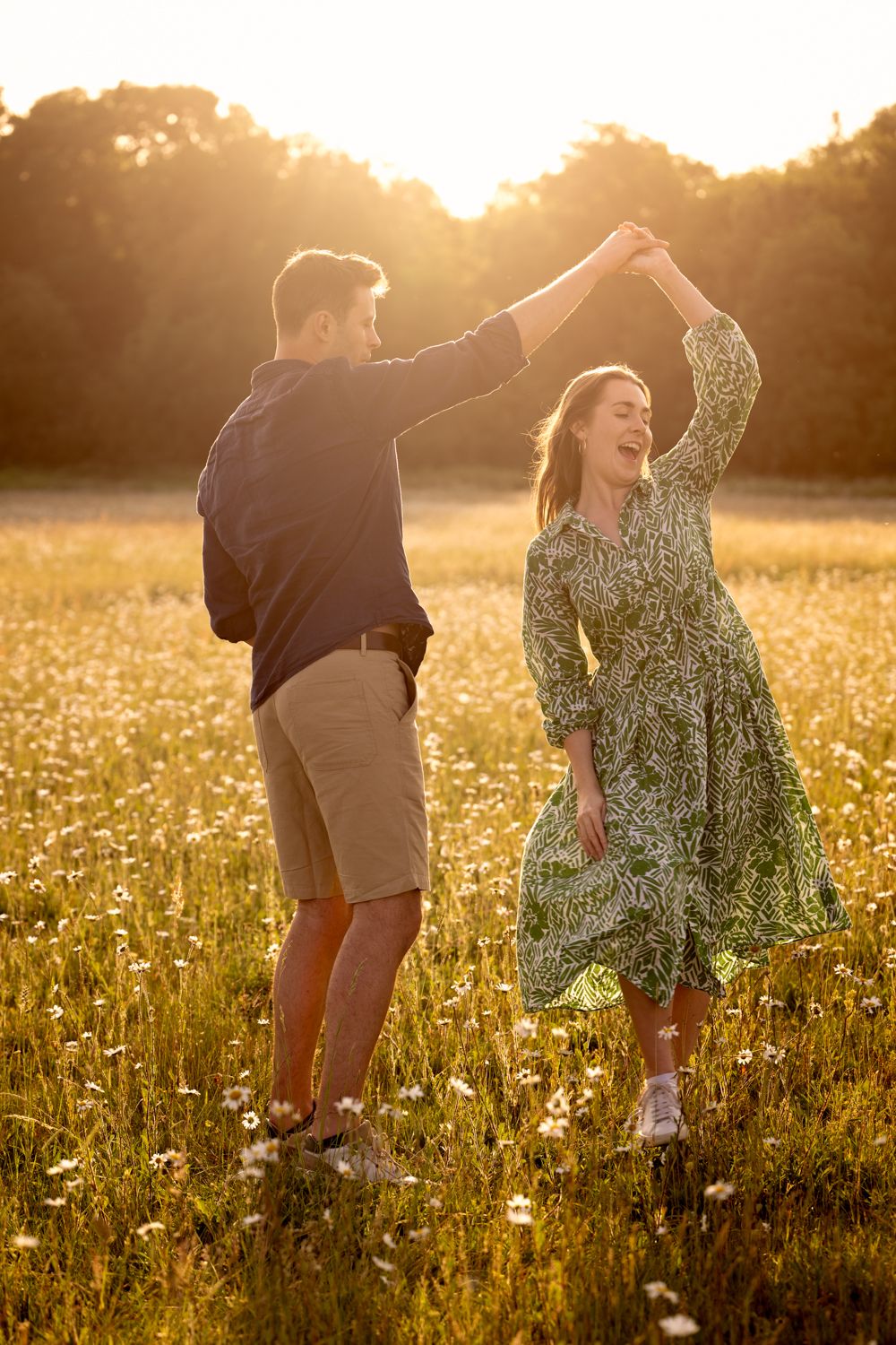 A couple dances joyfully in a golden wildflower meadow at sunset, creating a romantic silhouette against the warm light.