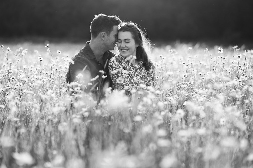 A romantic black and white photograph of a couple sitting together in a blooming wildflower meadow.