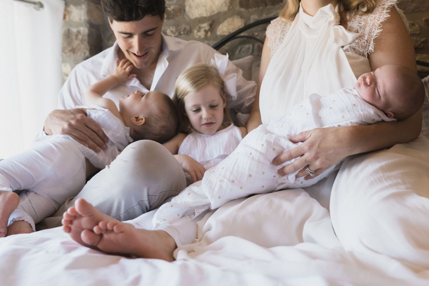 Documentary family photography showing parents relaxing on a bed with their newborn twins during an at home family session.