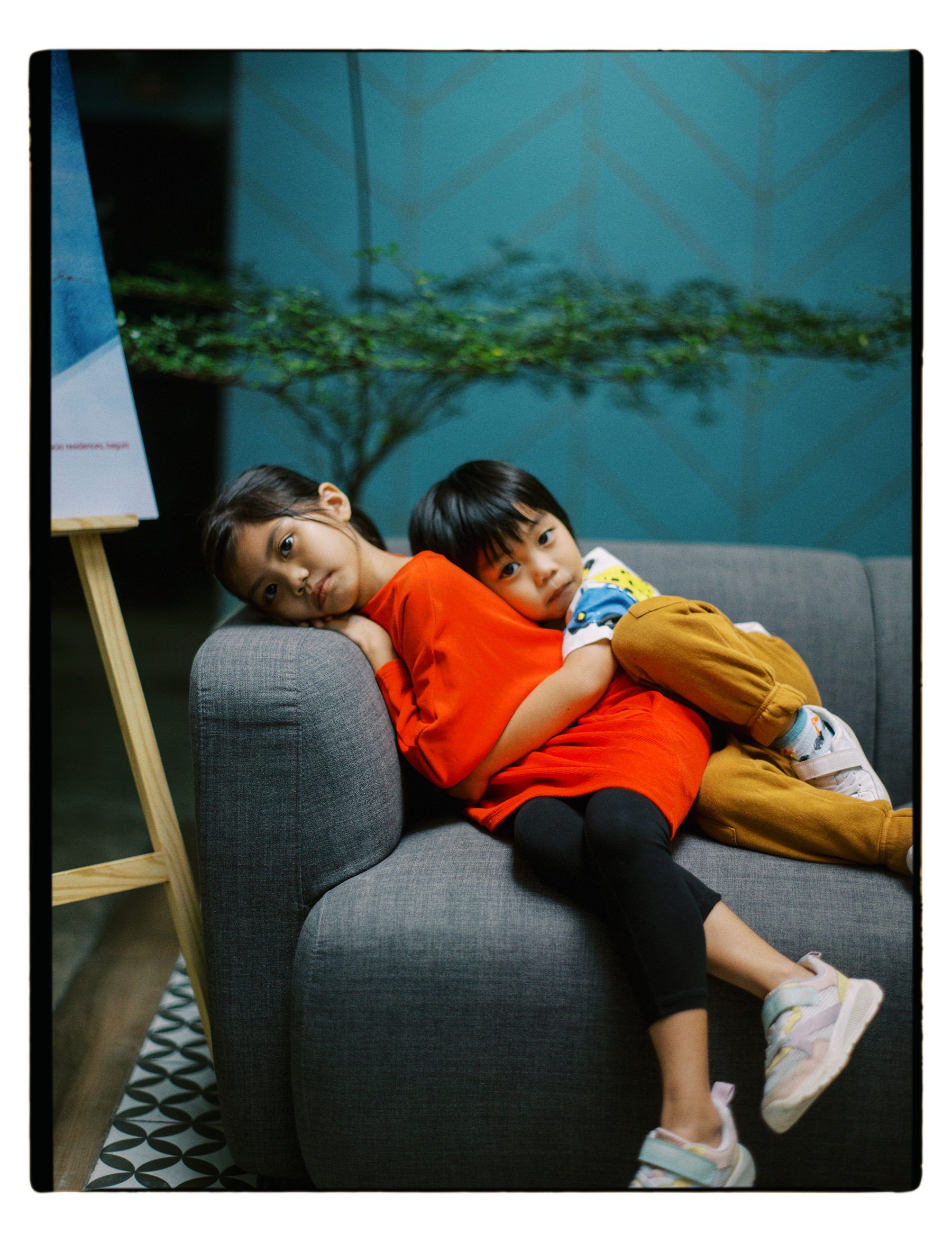 Two kids lounging on a gray couch in casual attire.