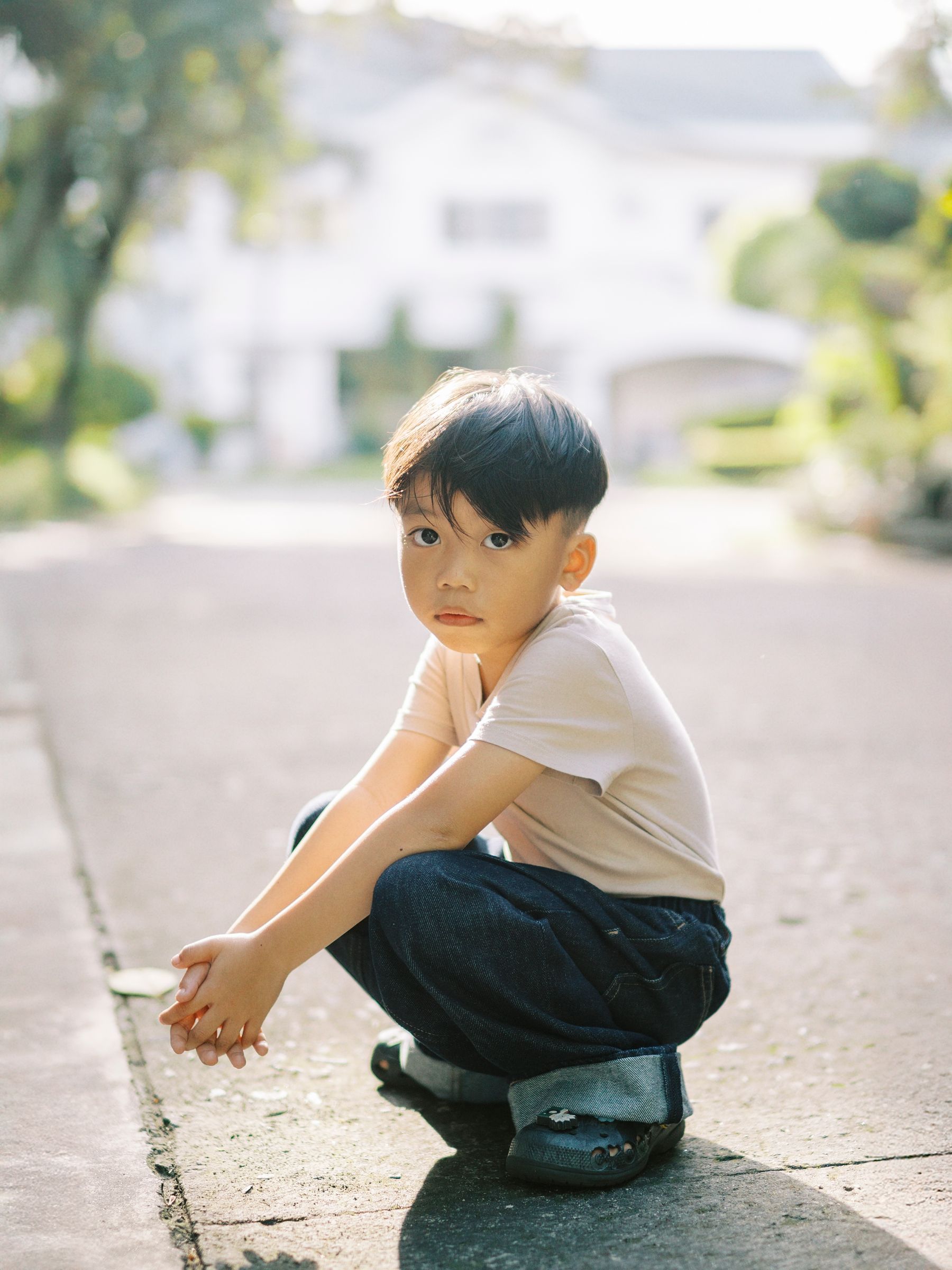 A child crouching on a suburban street in casual summer attire.