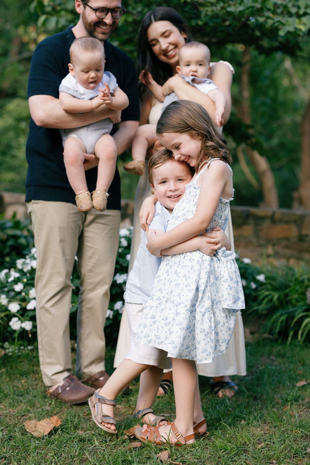 A family shares tender moments together in a garden setting with blooming white flowers and lush greenery.