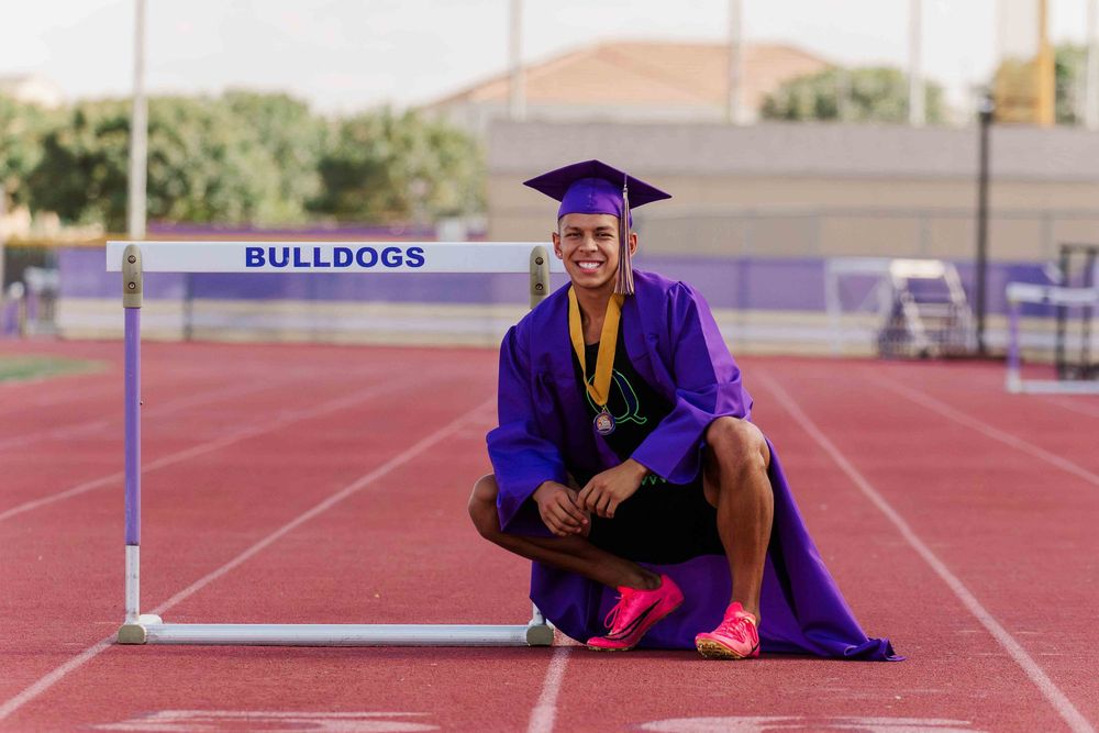 Track athlete stretches between purple hurdles on outdoor running track.