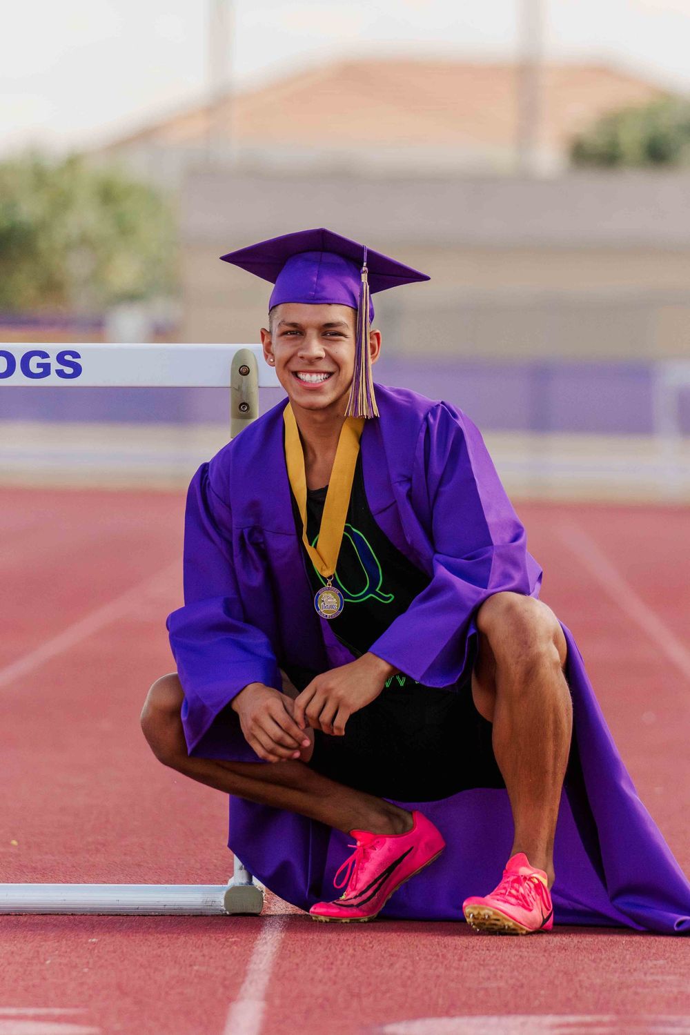 Graduate in purple cap and gown lying on red track surface during outdoor photo session.