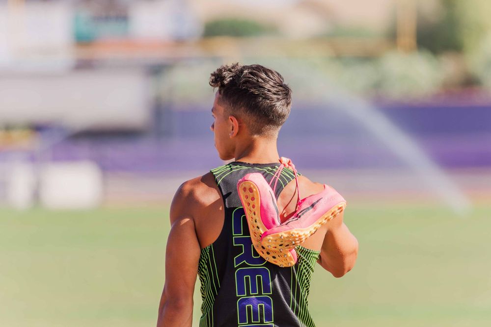 Athletic track runner stretching on outdoor running track during sunny day.