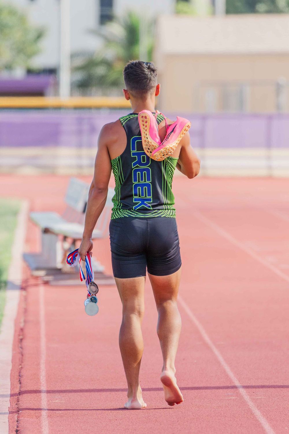 Runner in athletic gear training on red track with purple hurdles.