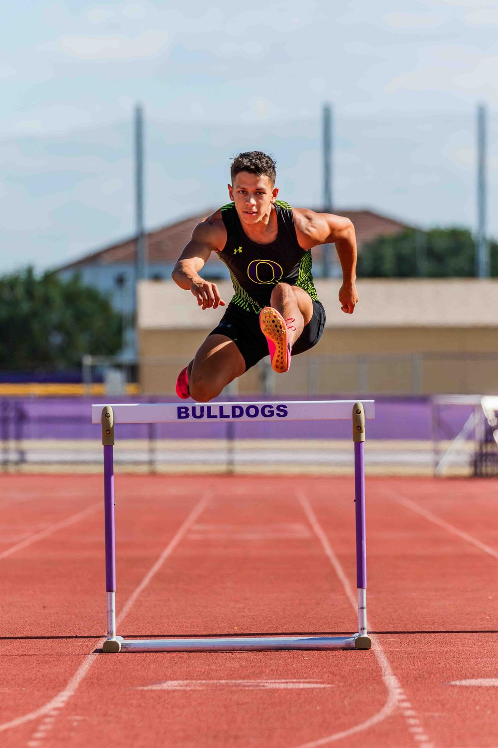 Athlete jumping over purple hurdles on a red running track during training.