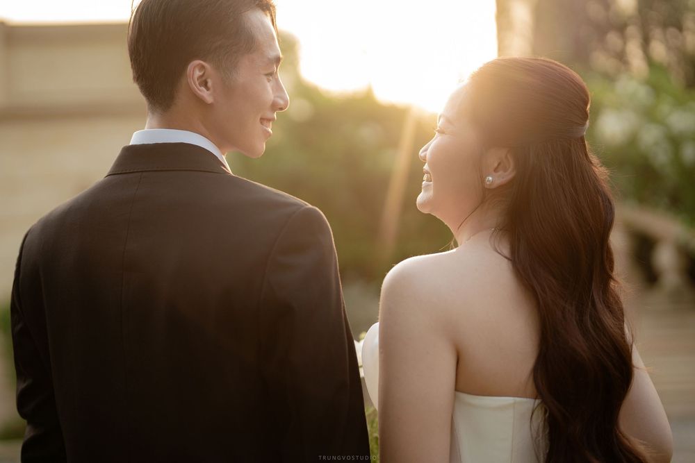 Asian bride and groom smiling at each other in warm golden sunset light during an outdoor wedding photoshoot.