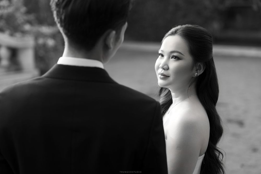 Black and white portrait of an Asian bride gazing back at her groom in a romantic outdoor pre-wedding photo.