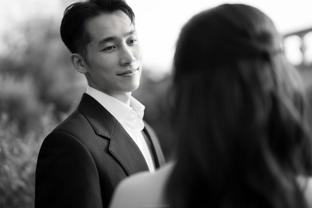 Black and white close-up of a smiling Asian groom in a suit looking at his bride during a wedding shoot.