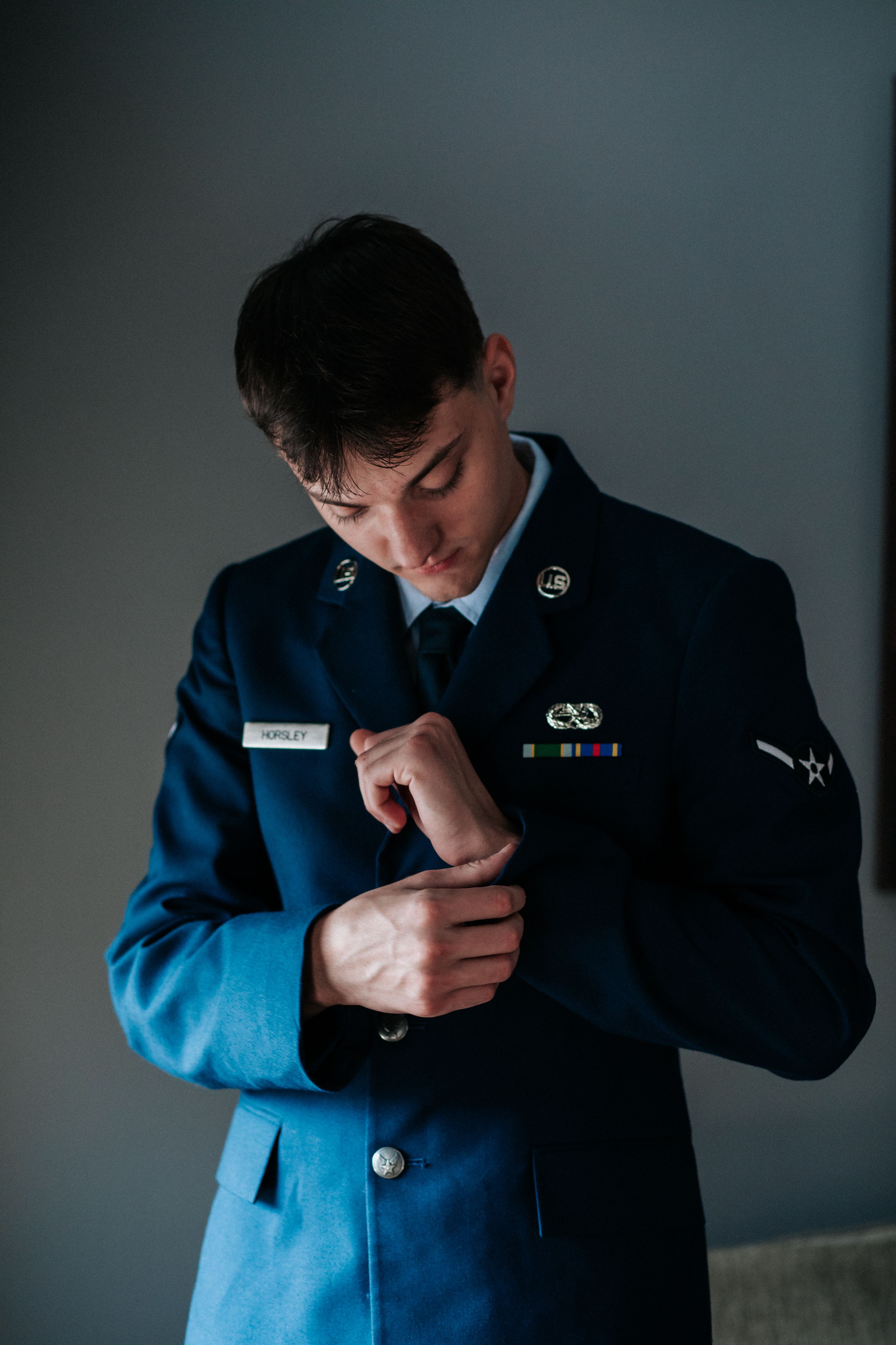 Dramatic moody portraits of a groom in a navy suit adjusting his tie.