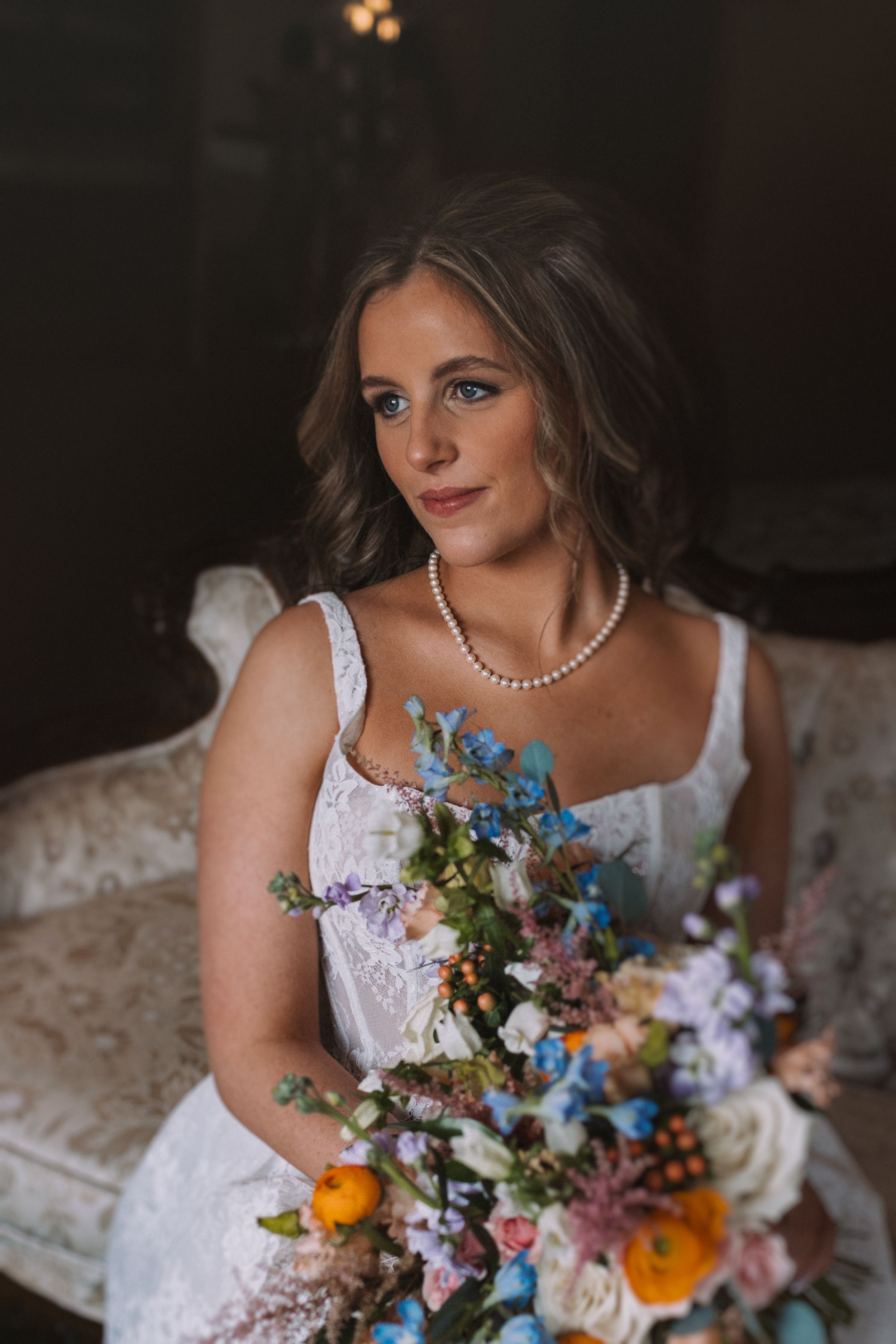 Moody bridal portraits featuring a pearl necklace and vibrant mixed flower bouquet.