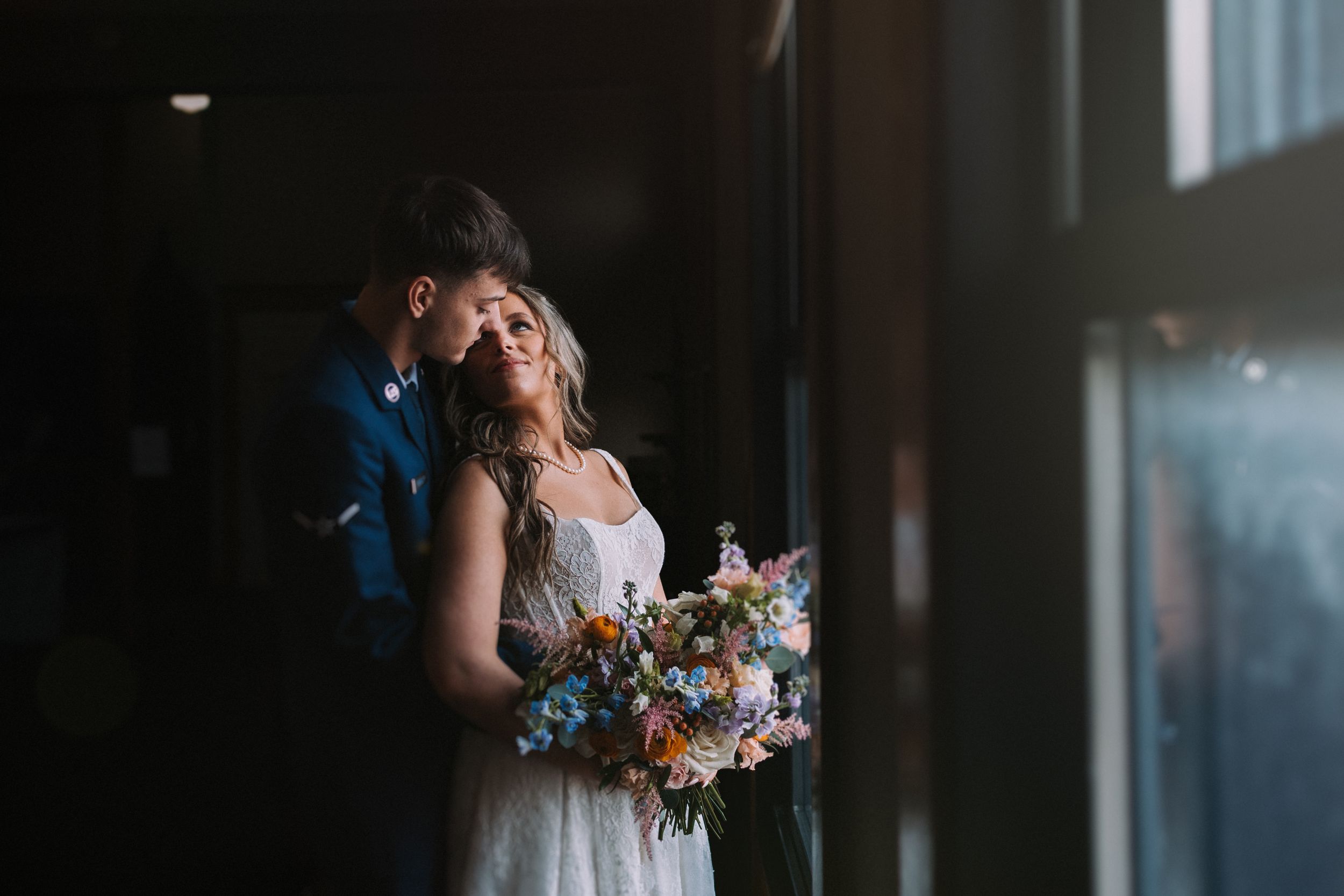 A romantic wedding moment captured in moody lighting with a colorful floral bouquet.