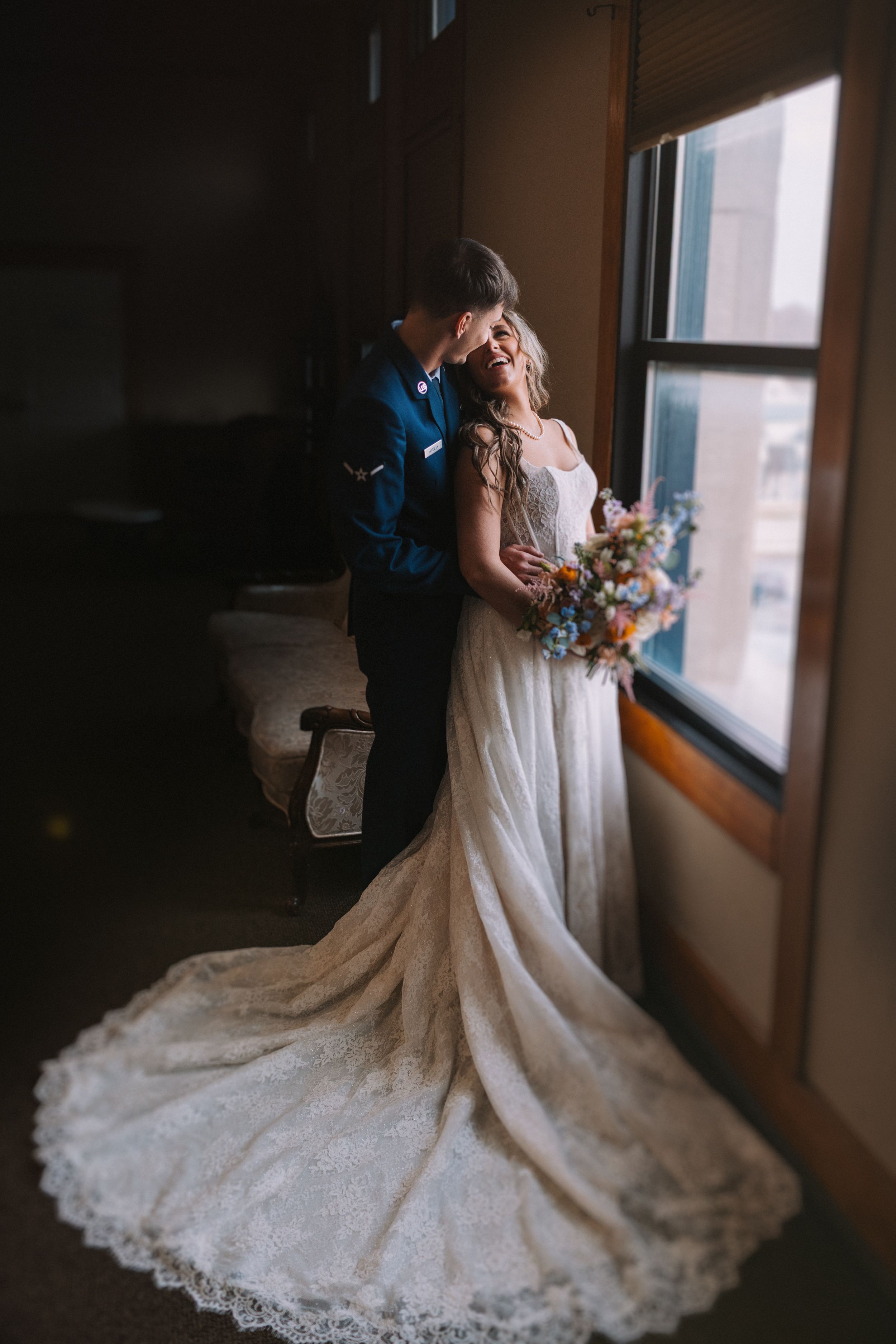 Silhouetted couple by window with bride's lace train flowing behind them.