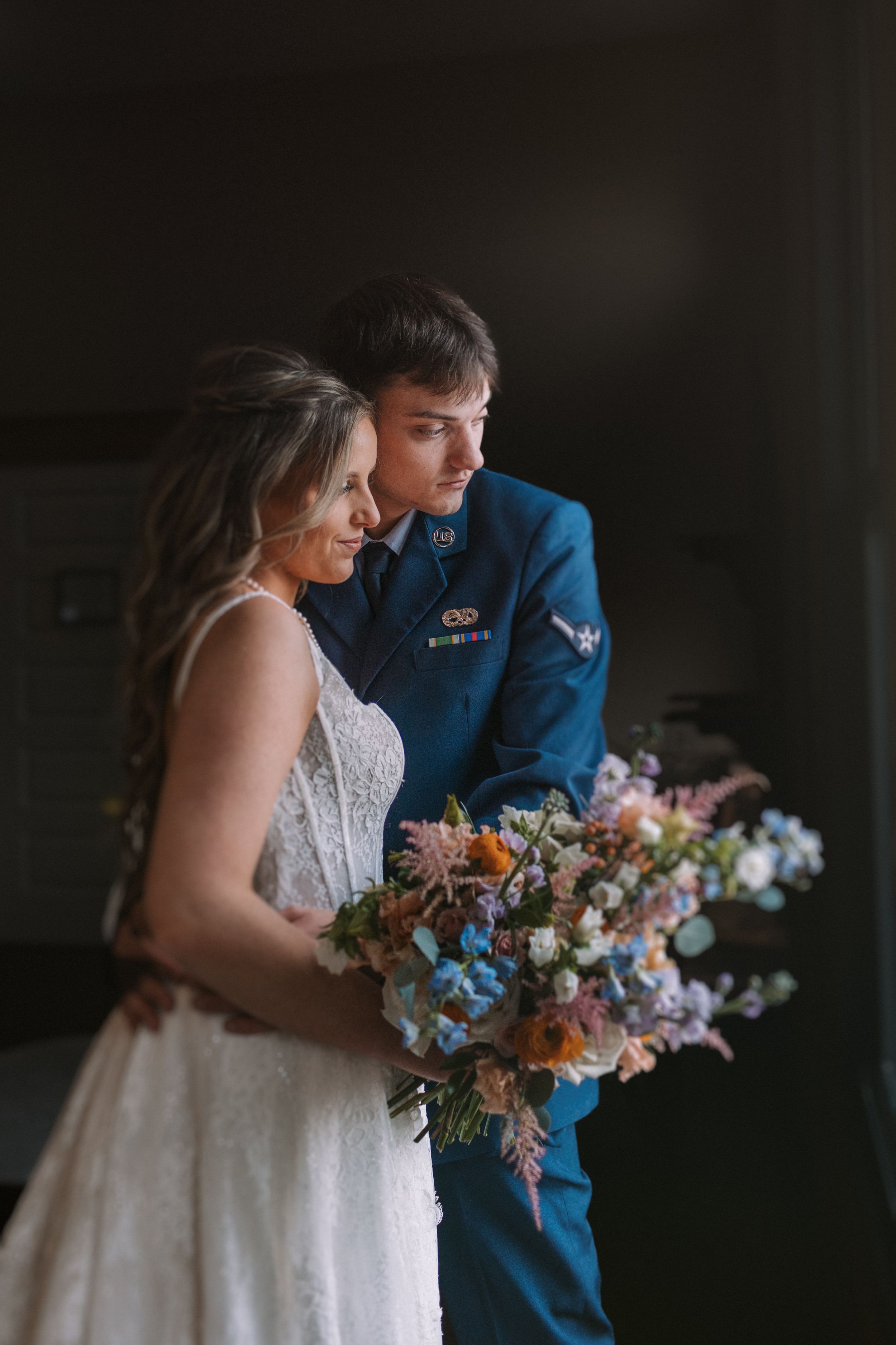 Military groom in blue uniform stands with bride holding vibrant wedding bouquet.