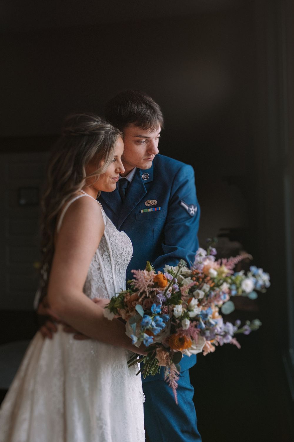 Military groom in blue uniform stands with bride holding vibrant wedding bouquet.