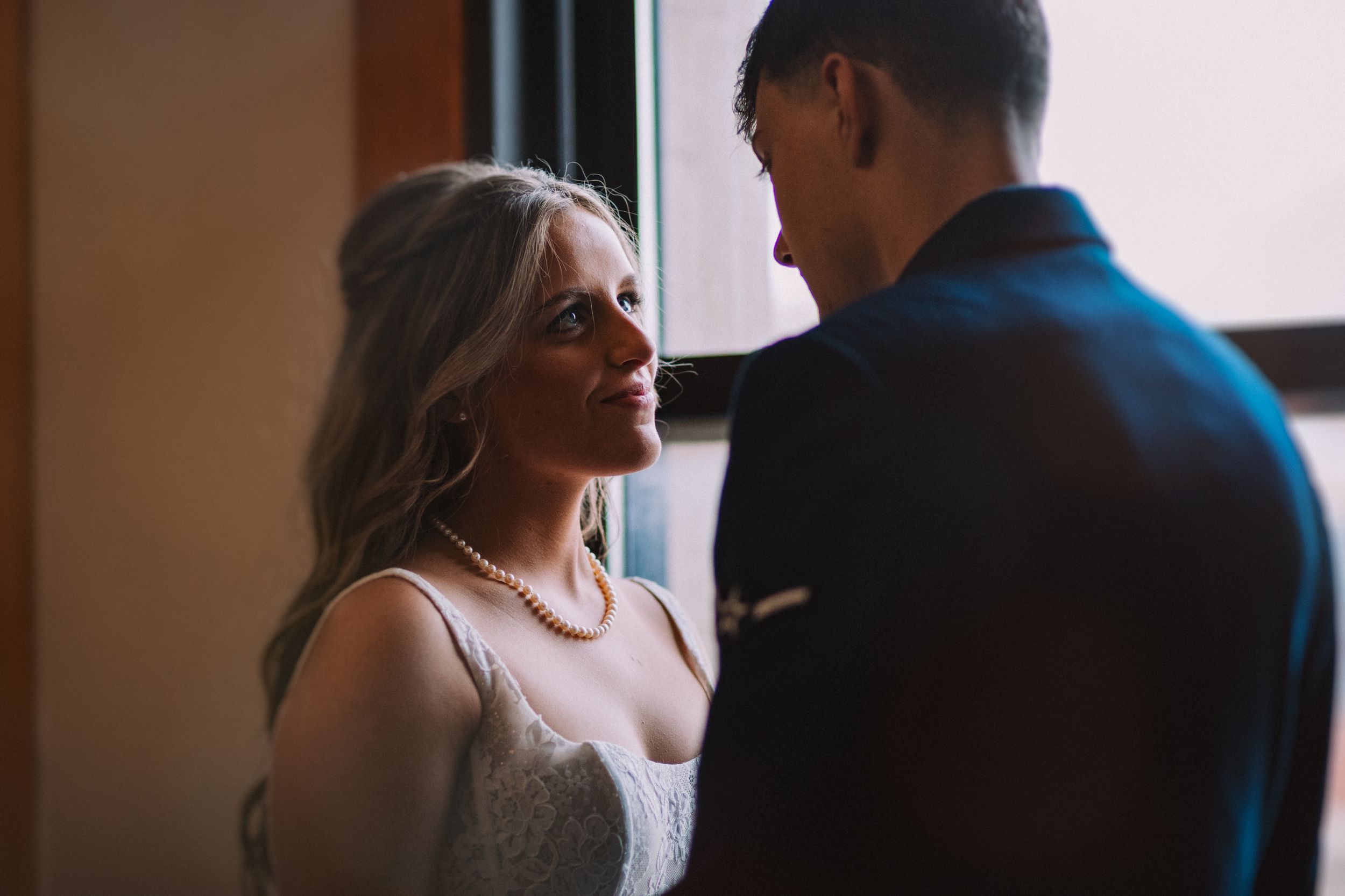 Couple shares intimate moment by window in wedding attire.