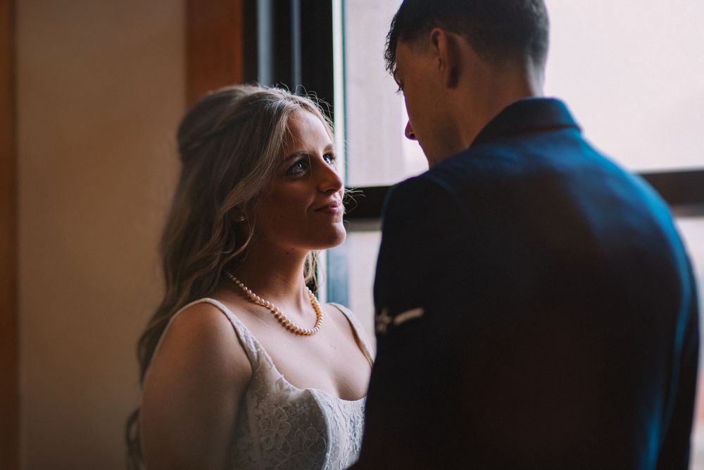 Couple shares intimate moment by window in wedding attire.