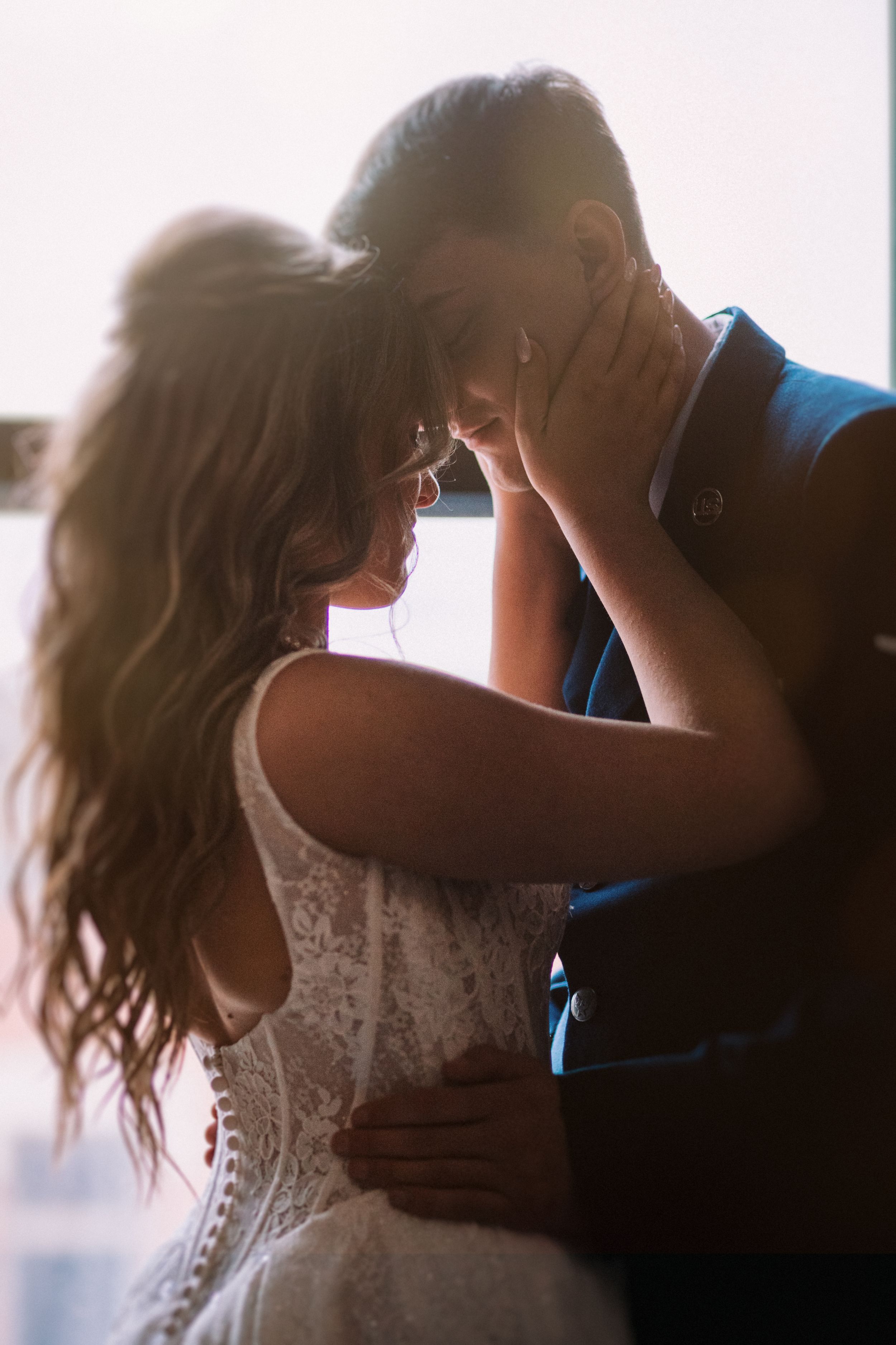 Backlit silhouette of couple sharing tender moment in wedding attire.