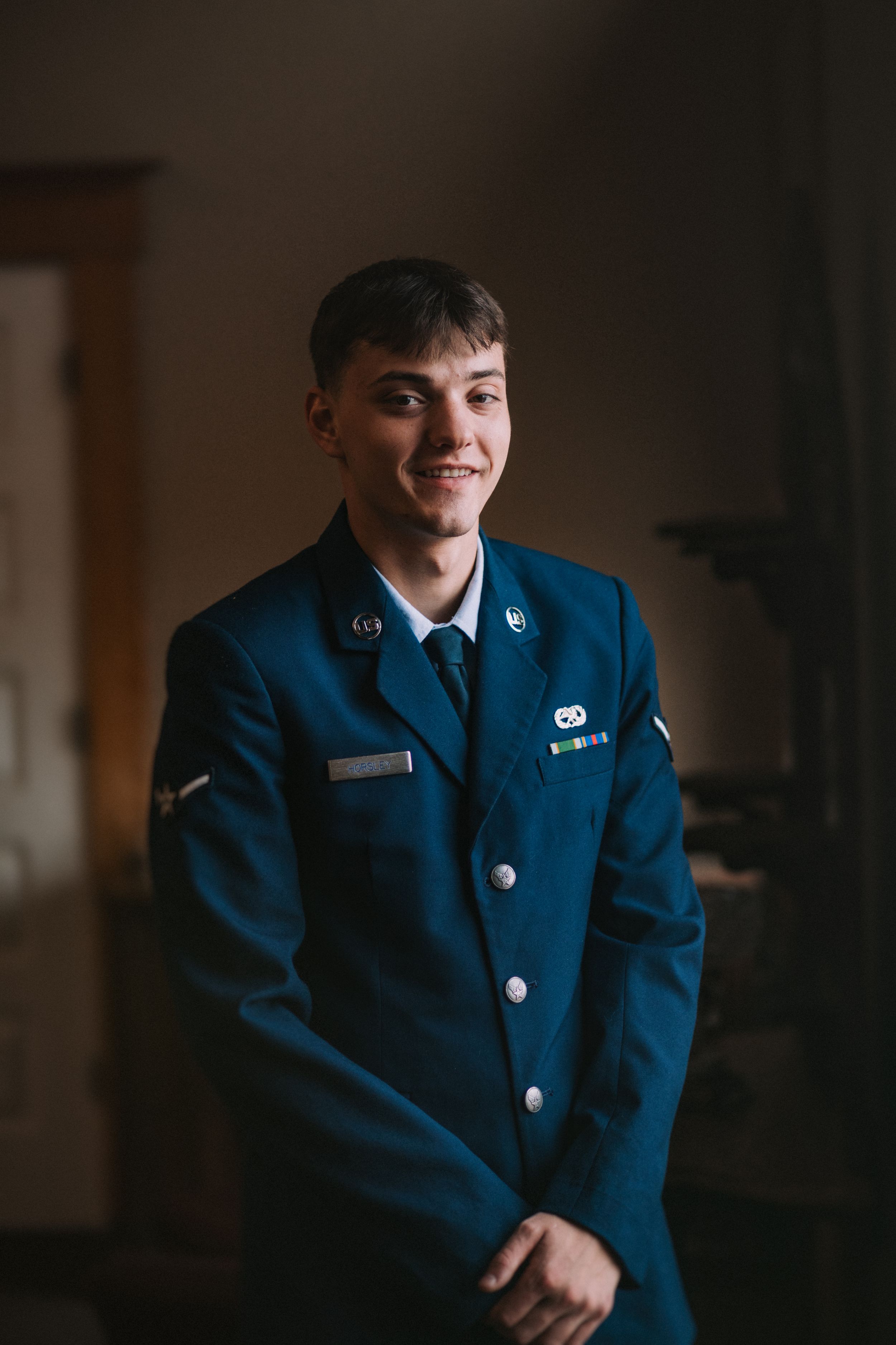 Military service member in dress blues poses for formal portraits in a dimly lit setting.