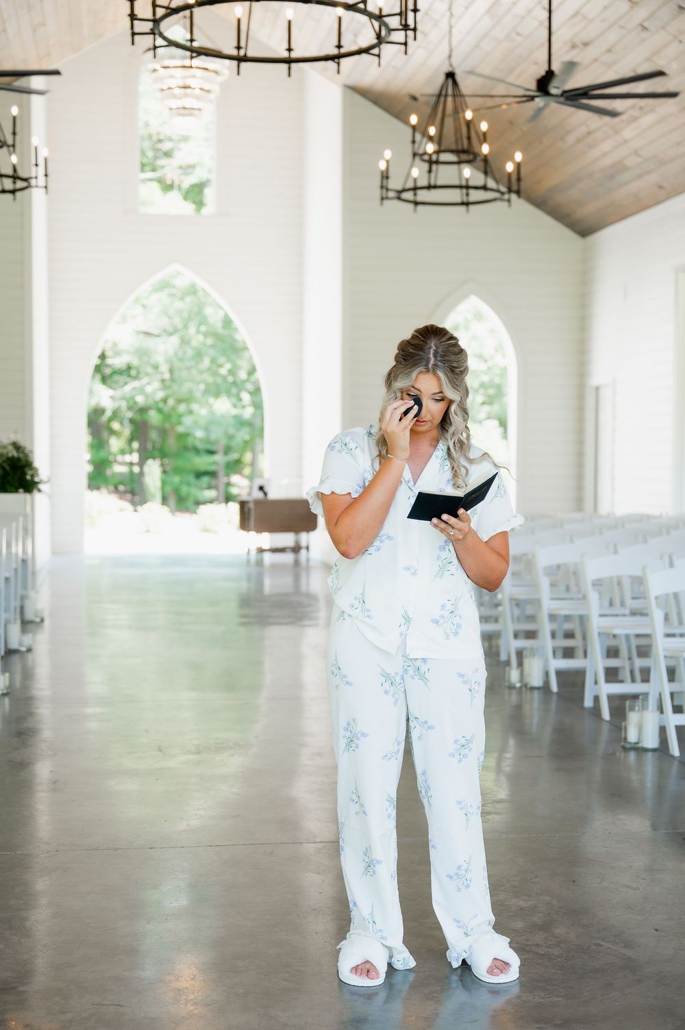 Empty wedding venue with white chairs and elegant chandeliers in bright indoor space.