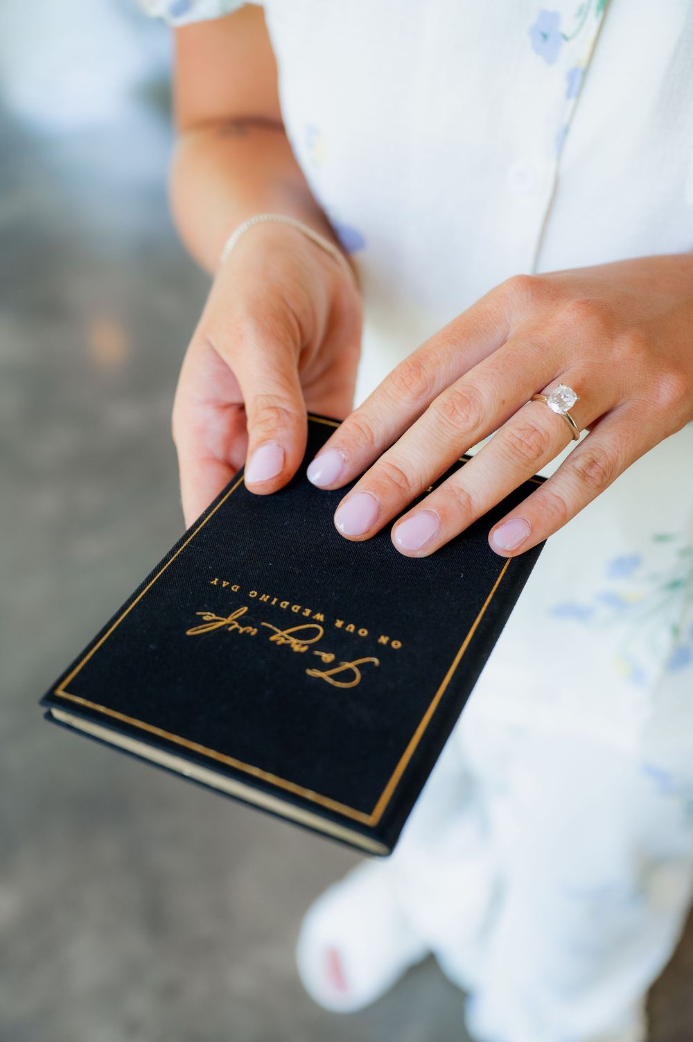 Hands holding black wedding vow books with gold lettering and engagement ring.