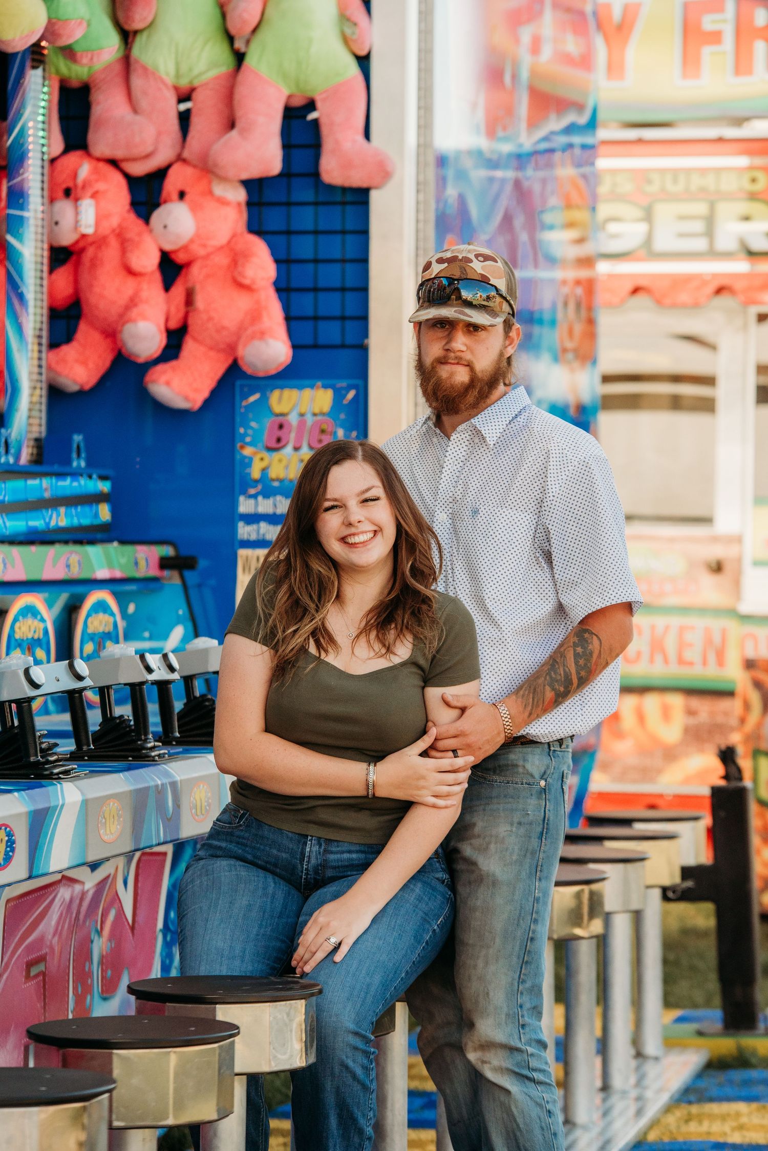 Couple enjoys romantic carnival date with colorful games and prizes in background at local fairground.
