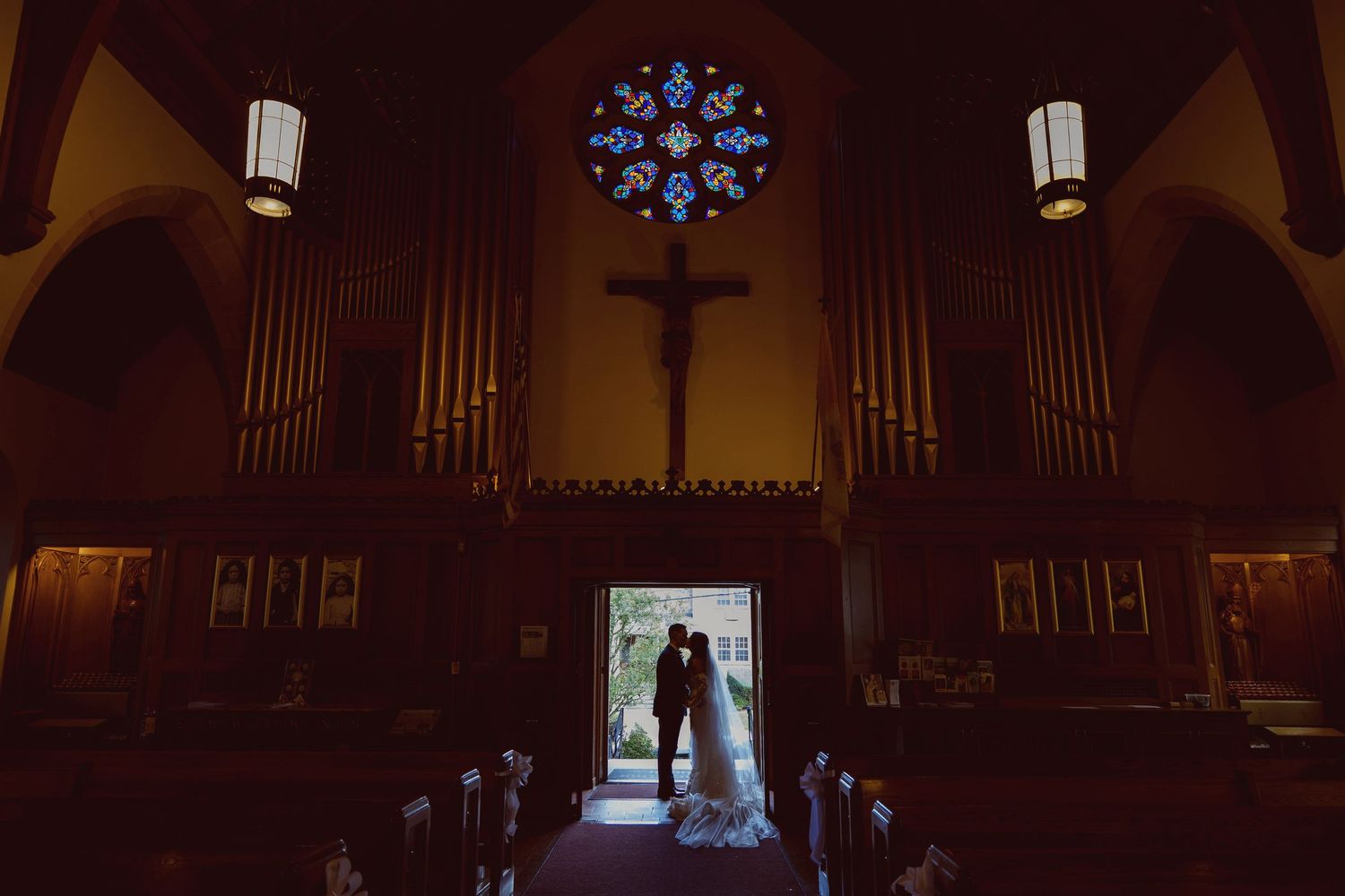 A dramatic wedding photo silhouette in a church with stained glass and organ pipes.