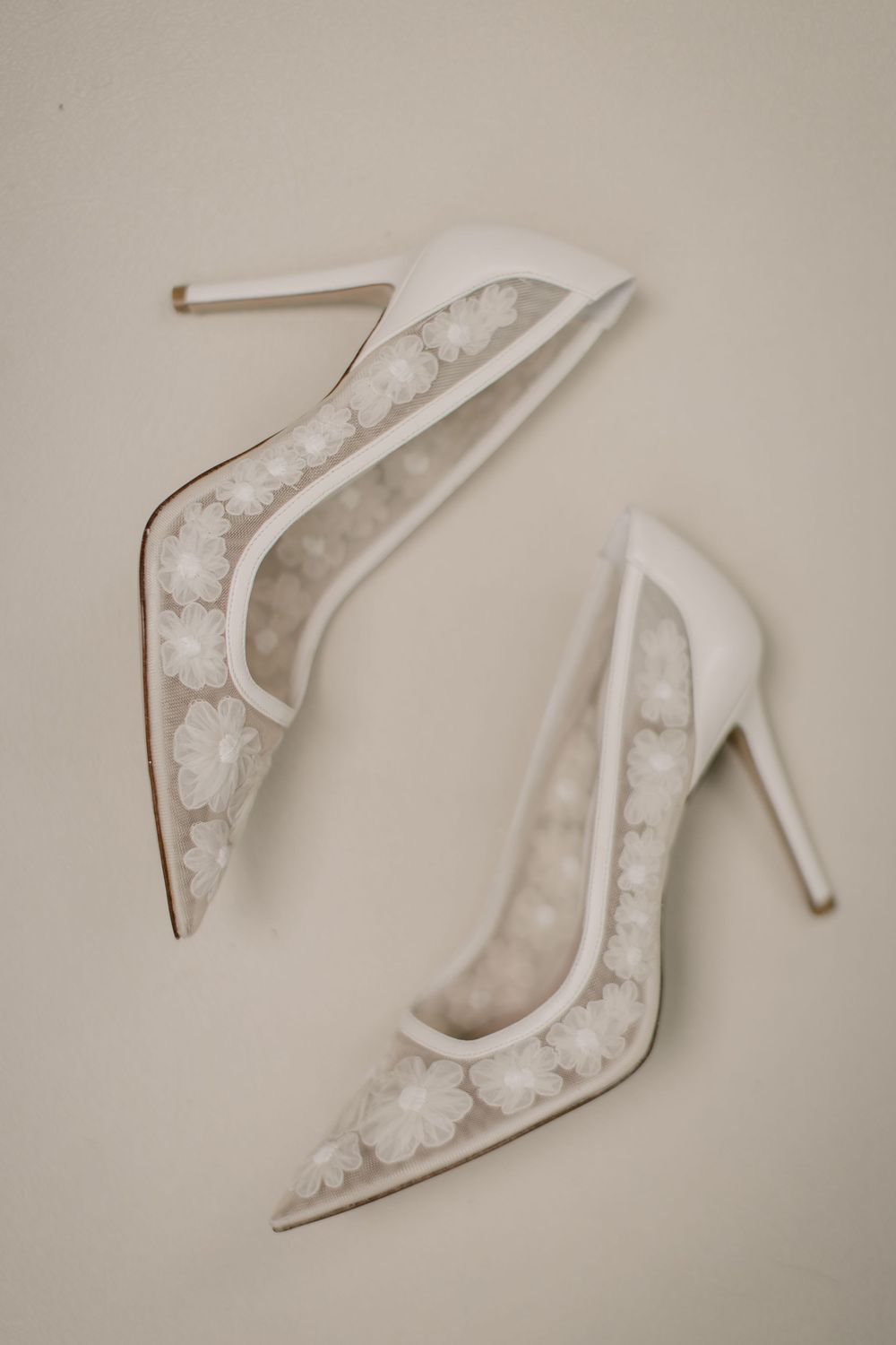 Elegant white lace bridal heels displayed against neutral background.