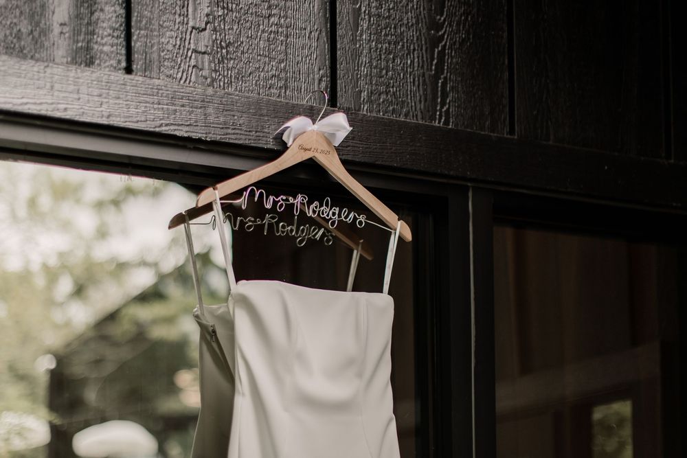 Wedding dress hanging on wooden hangers against a textured wall.