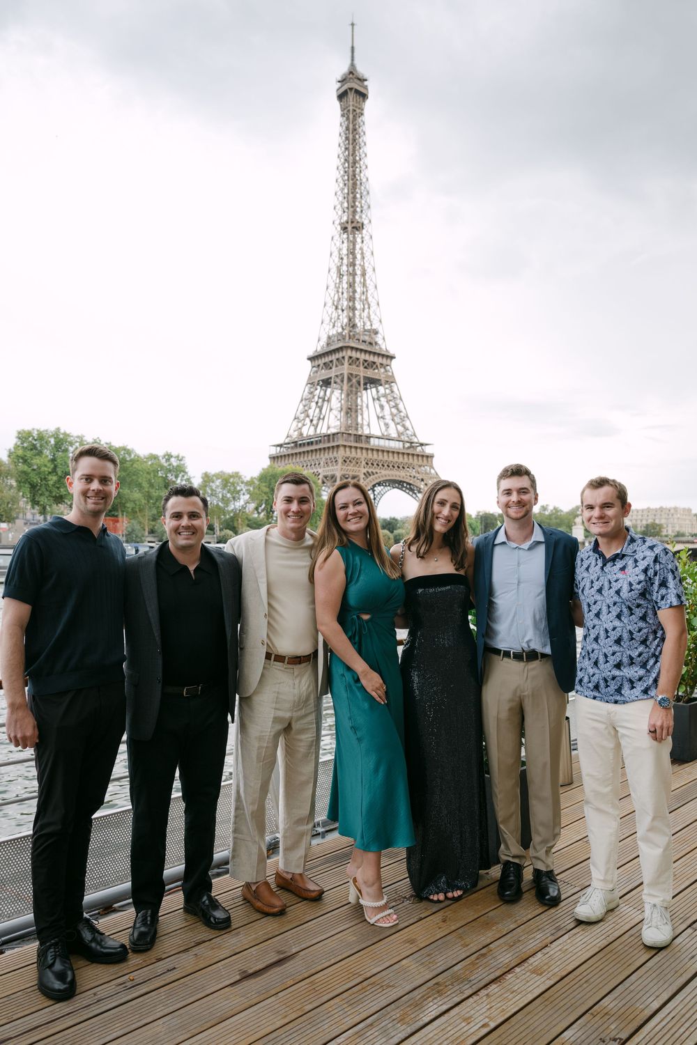 Group of friends posing together on a wooden deck with the Eiffel Tower visible in the background.