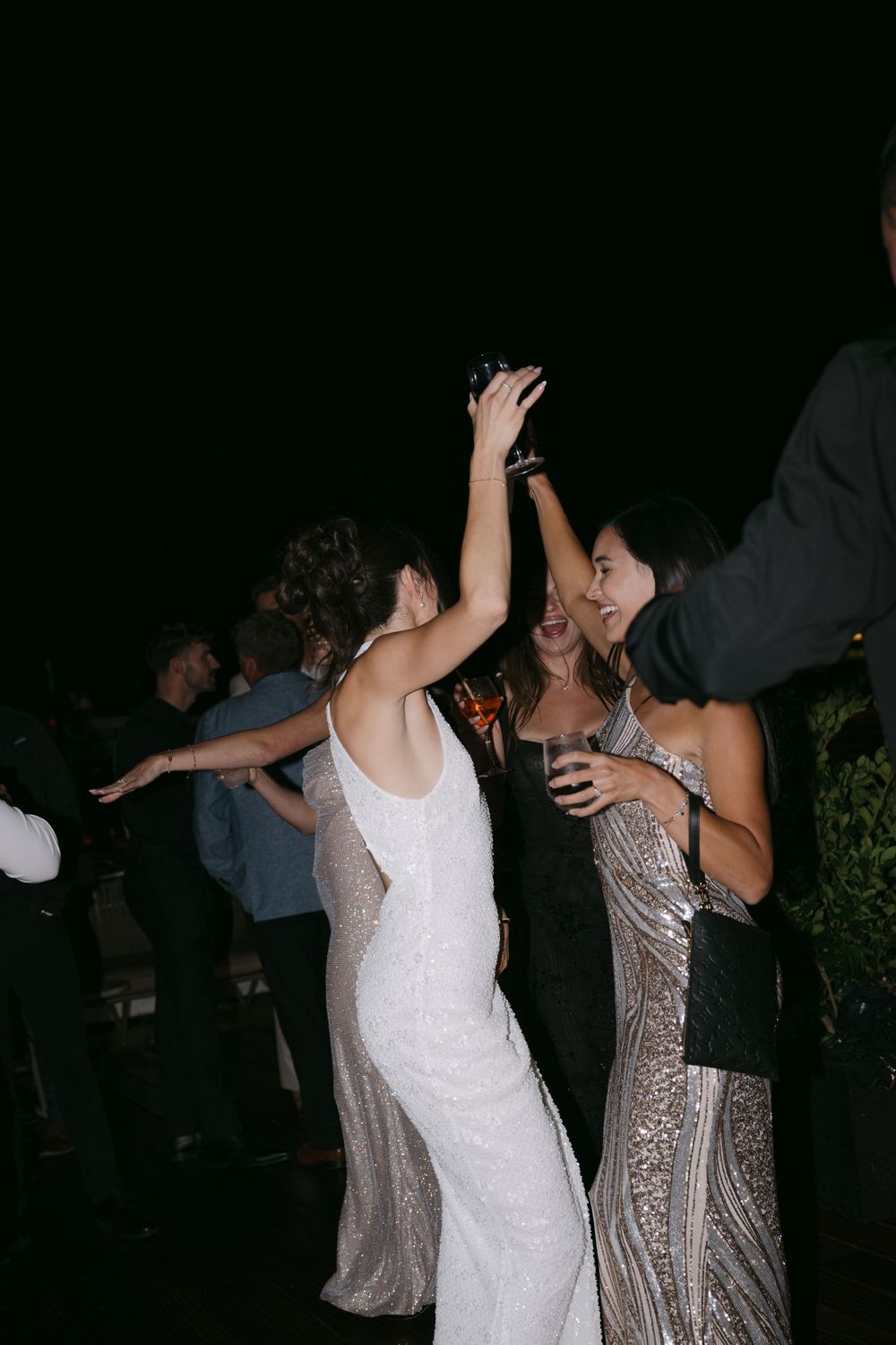 Two women in sparkly formal dresses dancing together at a nighttime celebration.