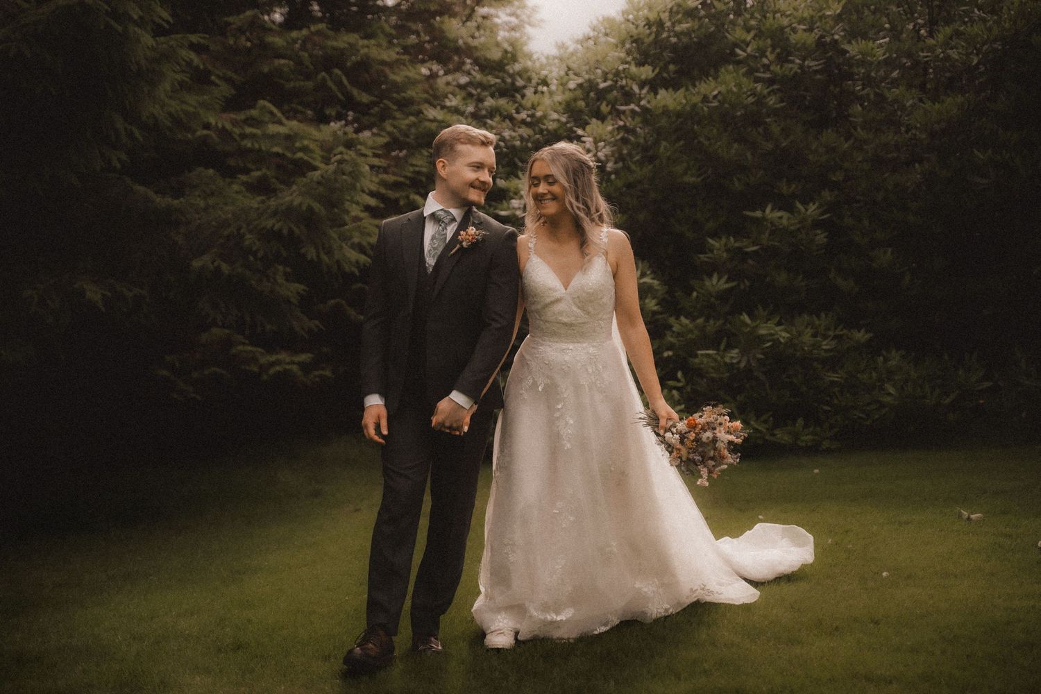 Romantic wedding couple poses in a lush green garden setting during golden hour.