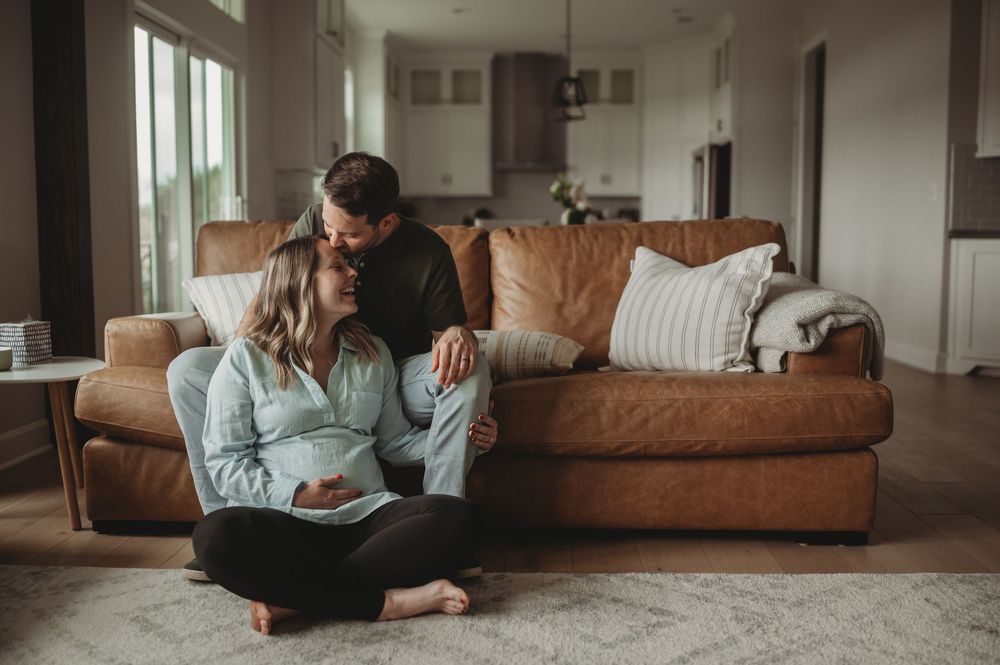 Pregnant couple sitting on living room floor, man kissing woman's head while she cradles her baby bump.