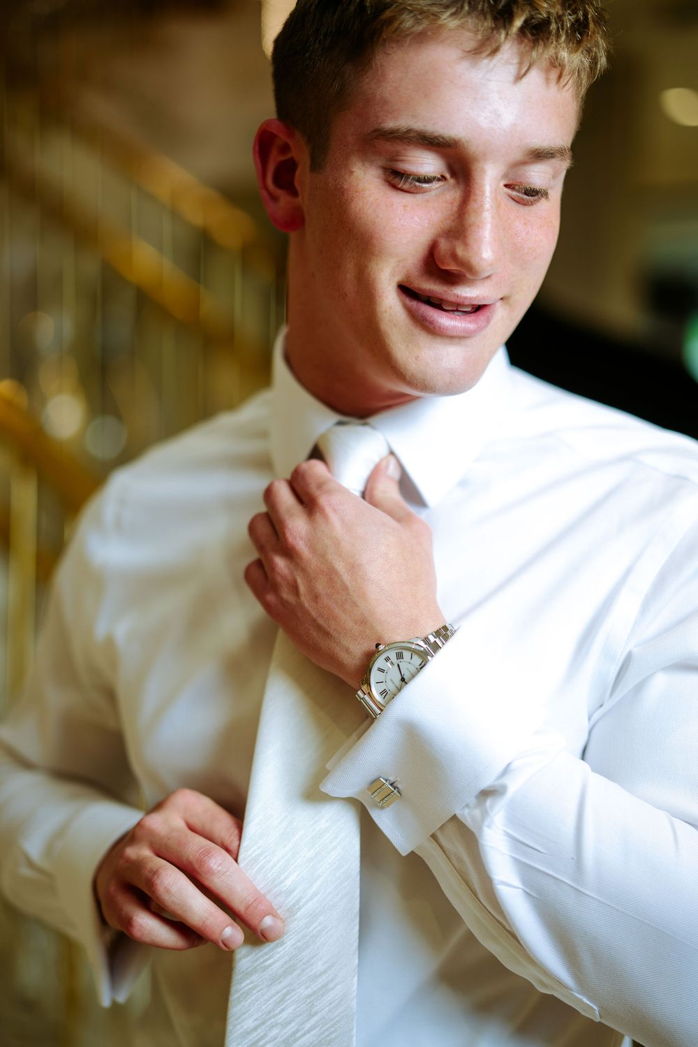A person in a white dress shirt adjusts their tie while getting ready.