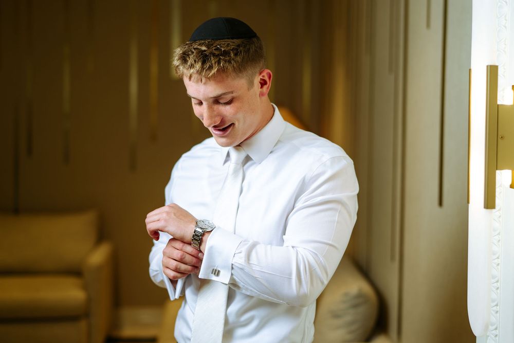 A person in a white dress shirt adjusts their cufflinks while getting ready.