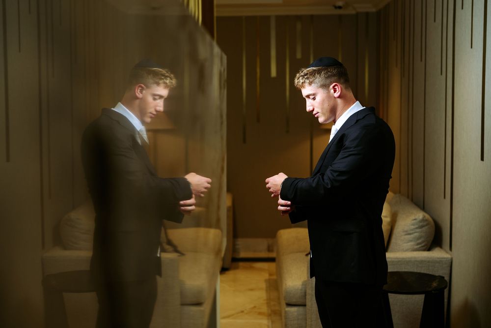Two people in formal attire stand facing each other in a warmly lit hallway with wood paneled walls.