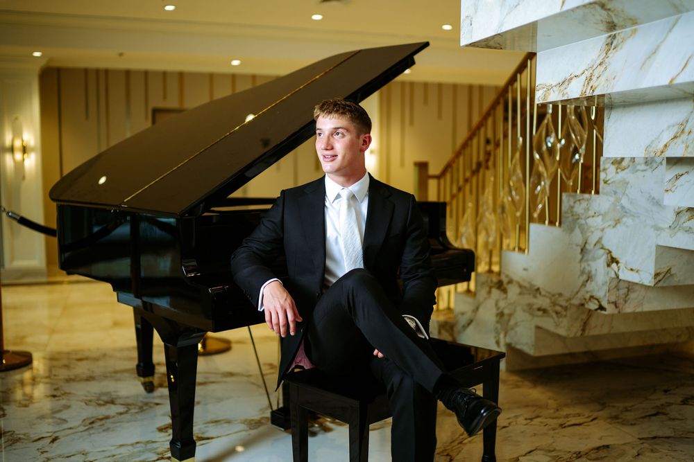 A grand piano sits elegantly in a luxurious marble-walled room with gold accents and dramatic lighting.