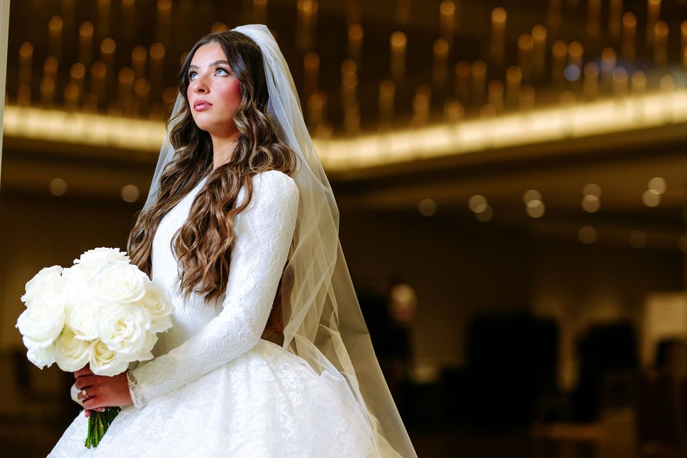 Dramatic wedding photos showing a bride in long sleeve lace dress holding white roses with bokeh lighting effects.