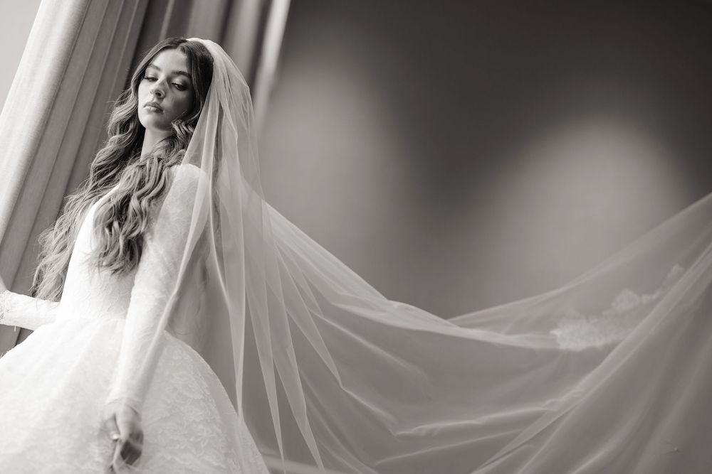 Ethereal bridal portrait with flowing veil creating dramatic movement in black and white.